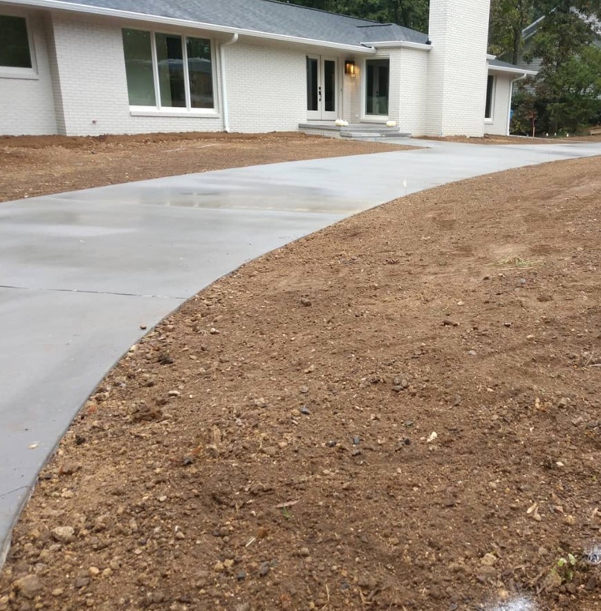 New curved concrete driveway with surrounding soil prepared for landscaping